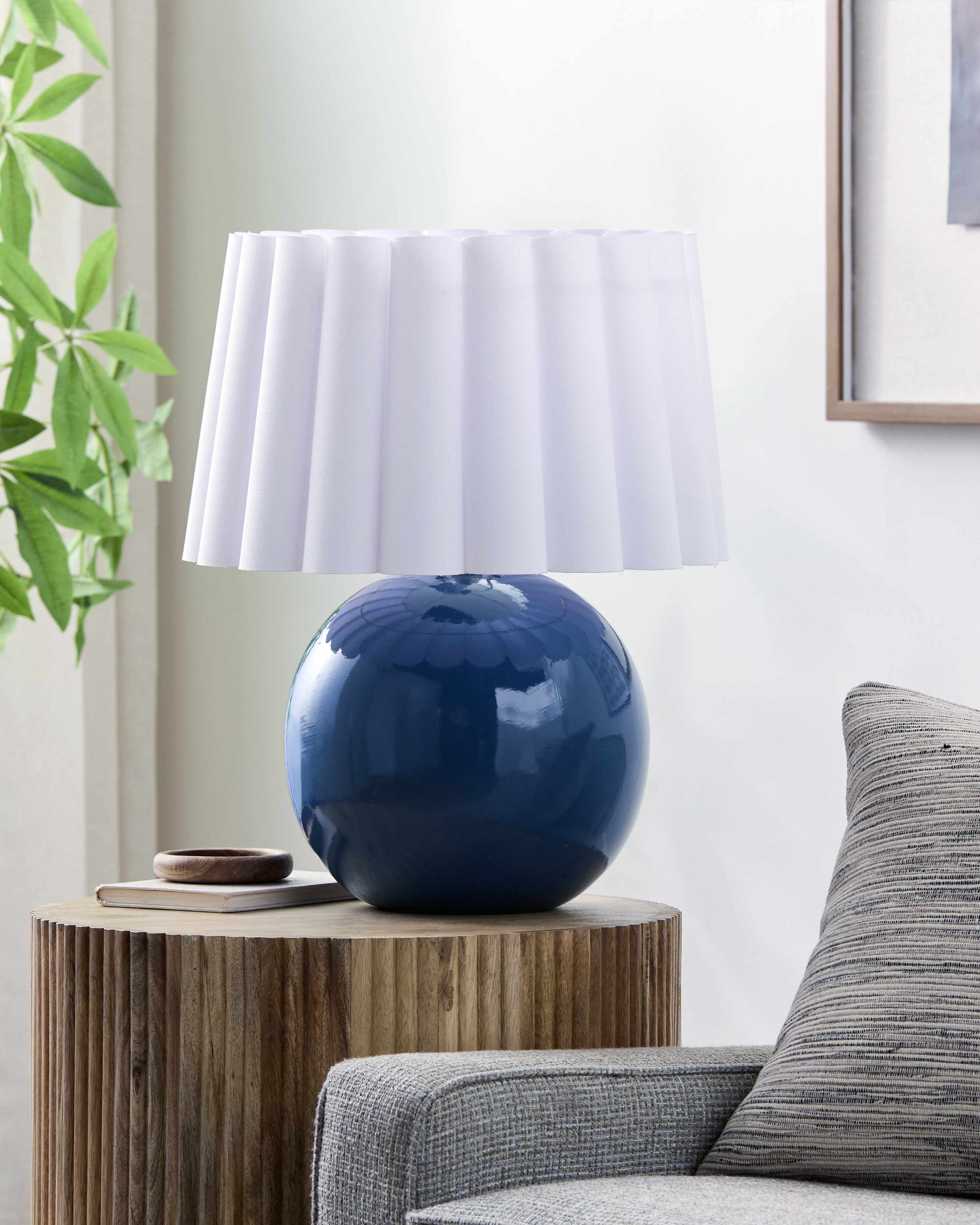 Blue spherical object on a wooden side table next to a gray sofa with a white lamp in the background.