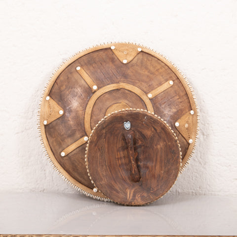 Wooden wall art piece with circular design on a textured white wall