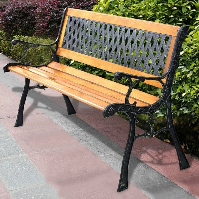Wooden bench with black metal frame on a paved area with greenery in the background