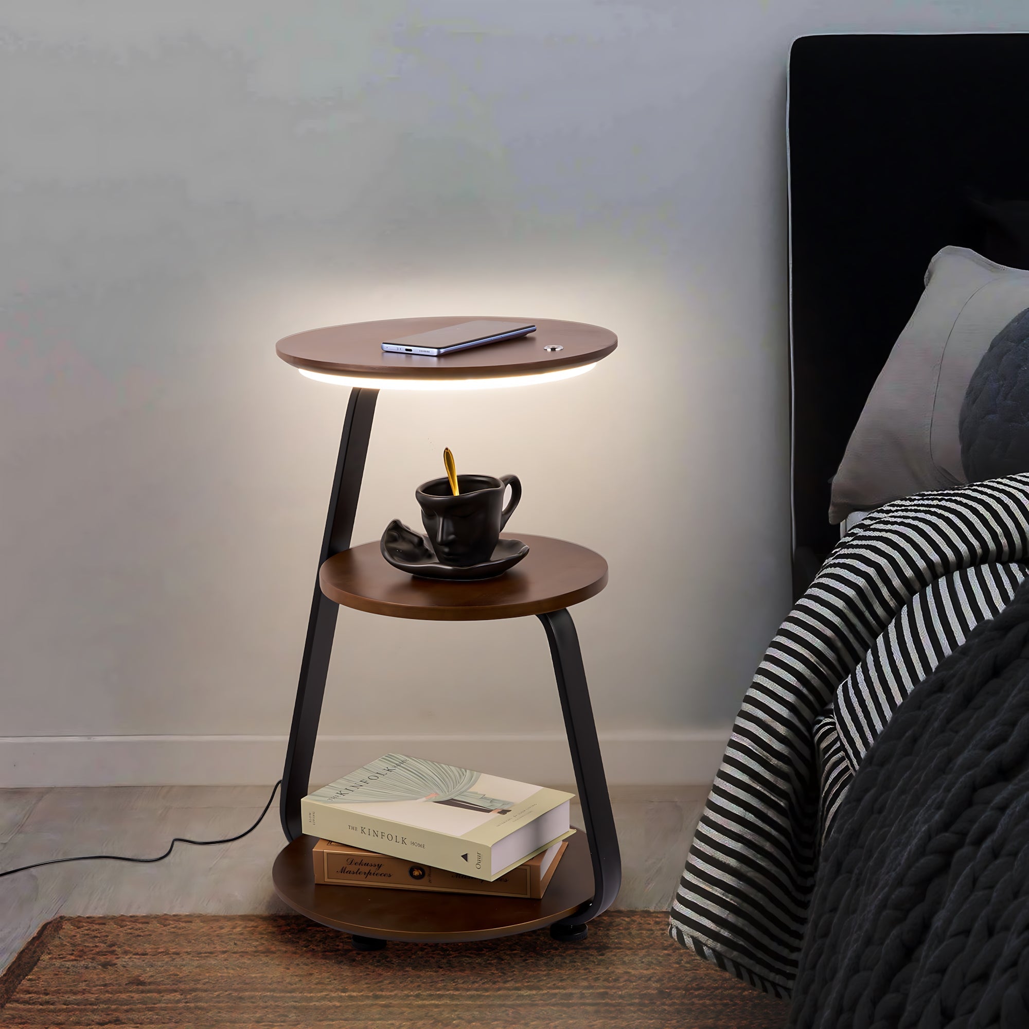 Wooden nightstand with a lamp, mug, and books next to a bed.