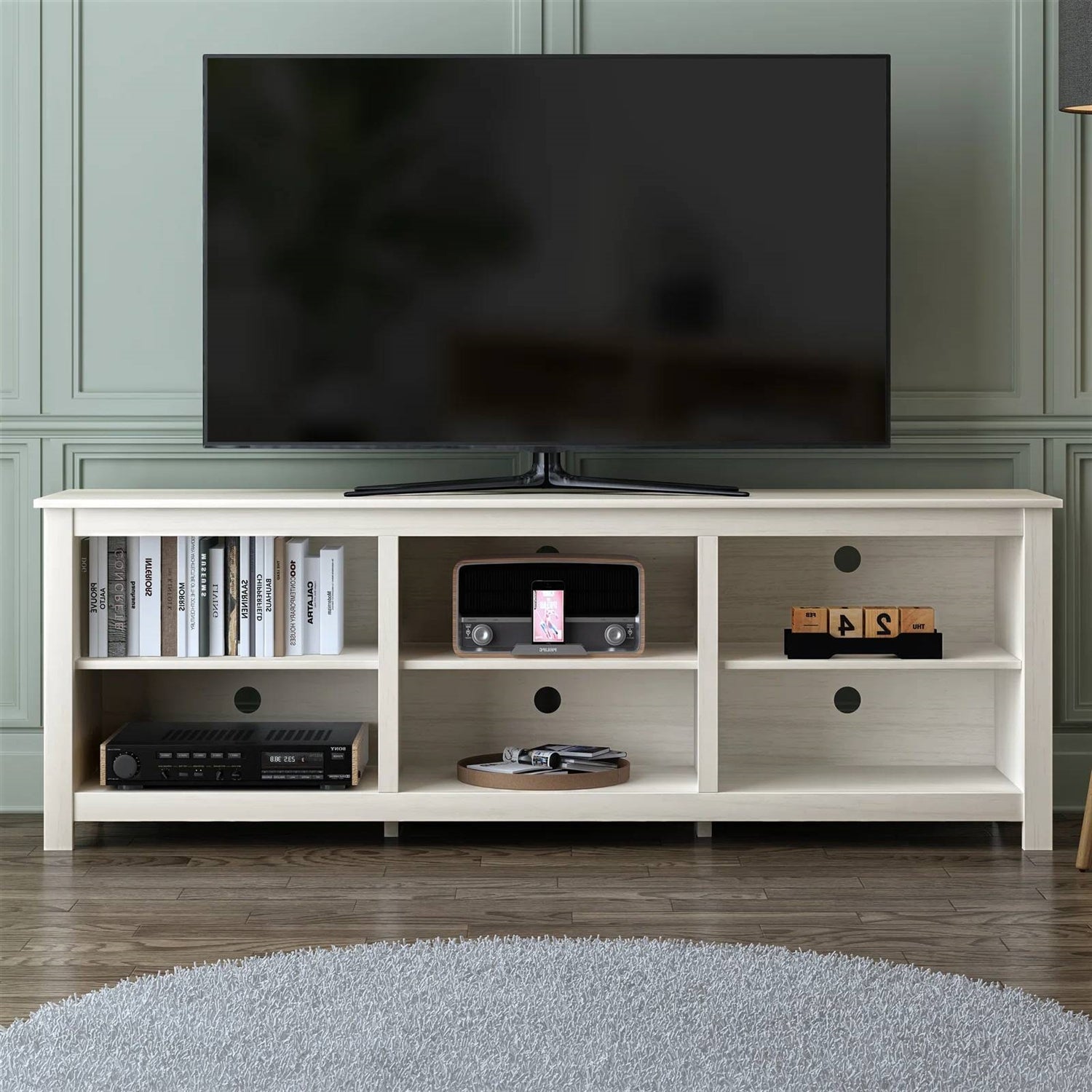 TV on a white entertainment console with shelves against a wall.