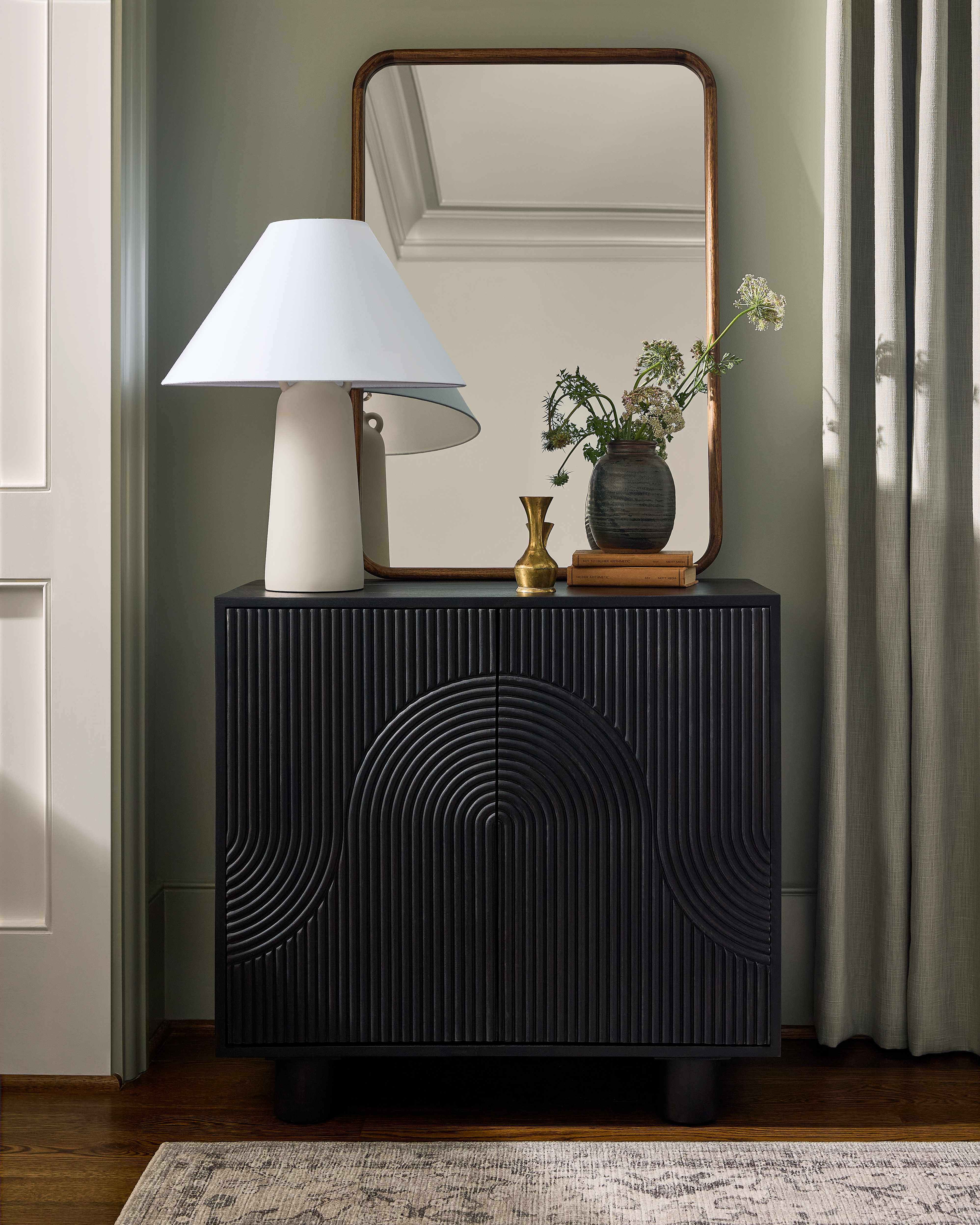 Black textured side table with a lamp, mirror, and decorative items in a room.