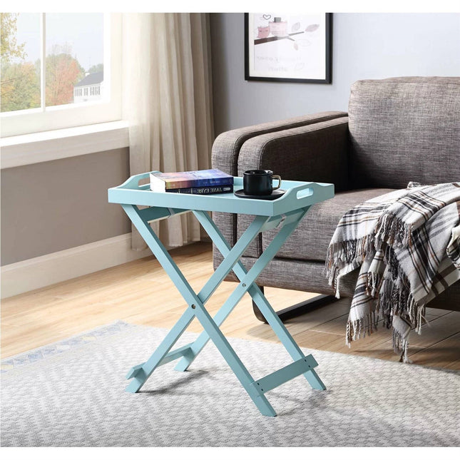 Light blue folding side table with books and a mug in a living room setting.