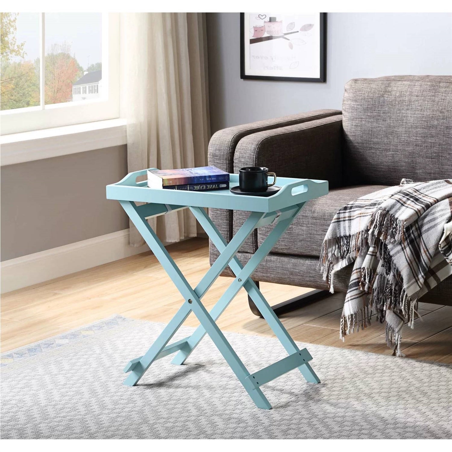 Light blue folding side table with books and a mug in a living room setting.