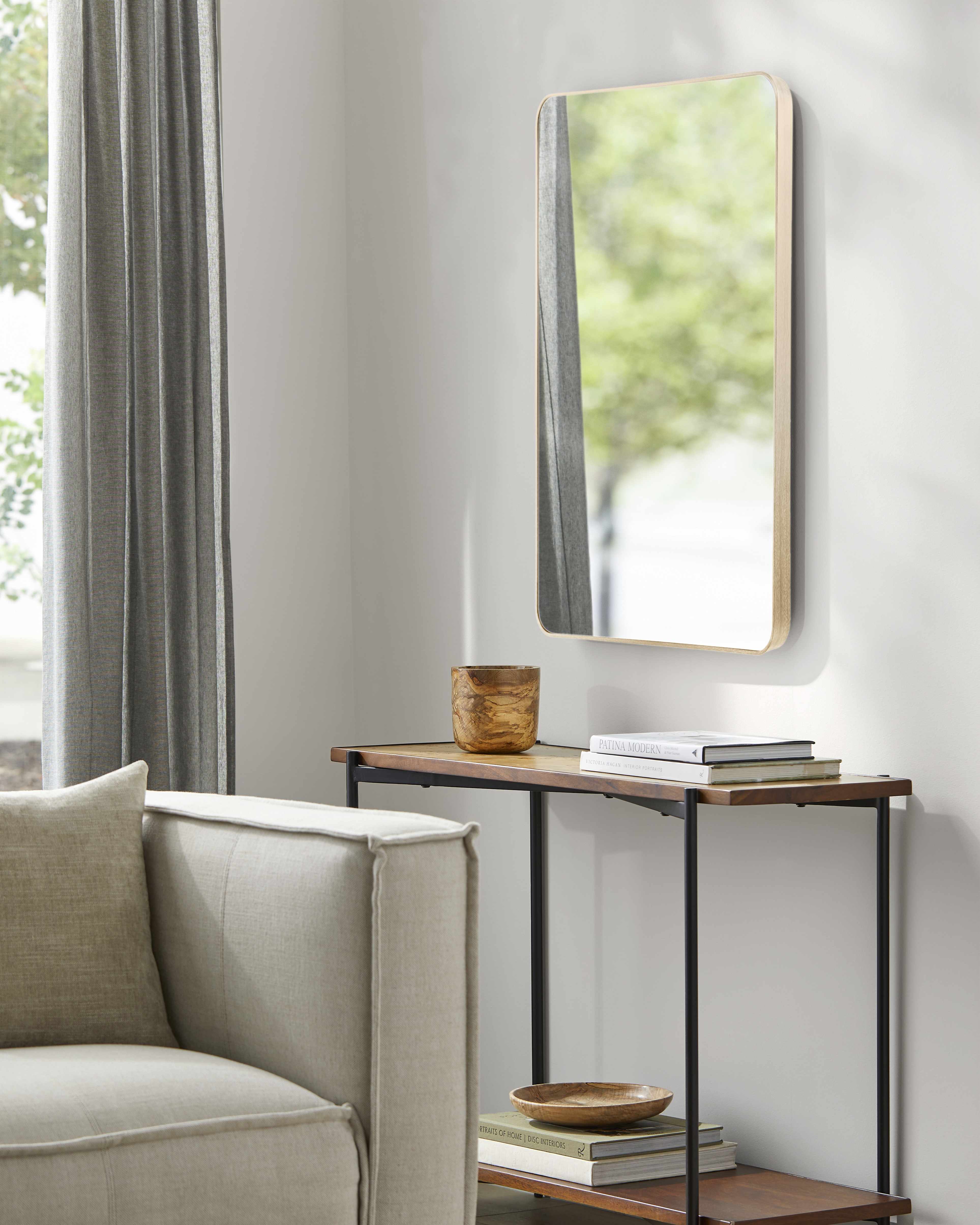Small table with decorative items next to a mirror on a wall, with a chair and window in the background.