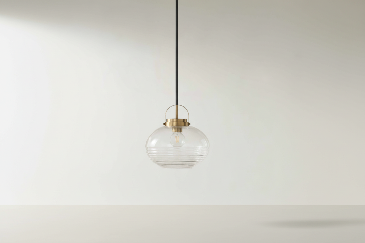 Pendant light with clear glass shade and gold fixture on a white wall.