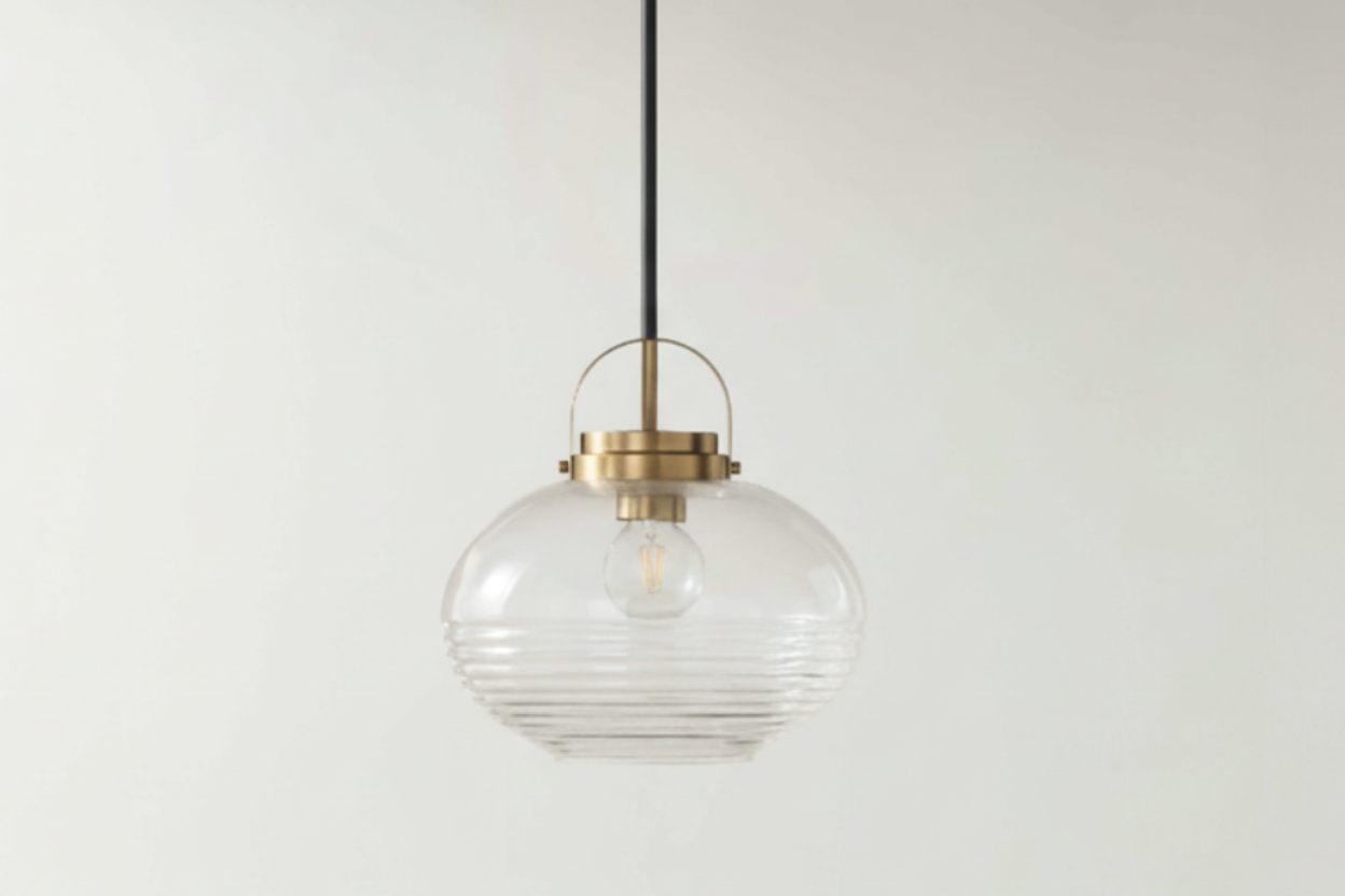 Pendant light with clear glass shade and gold fixture on a white wall.