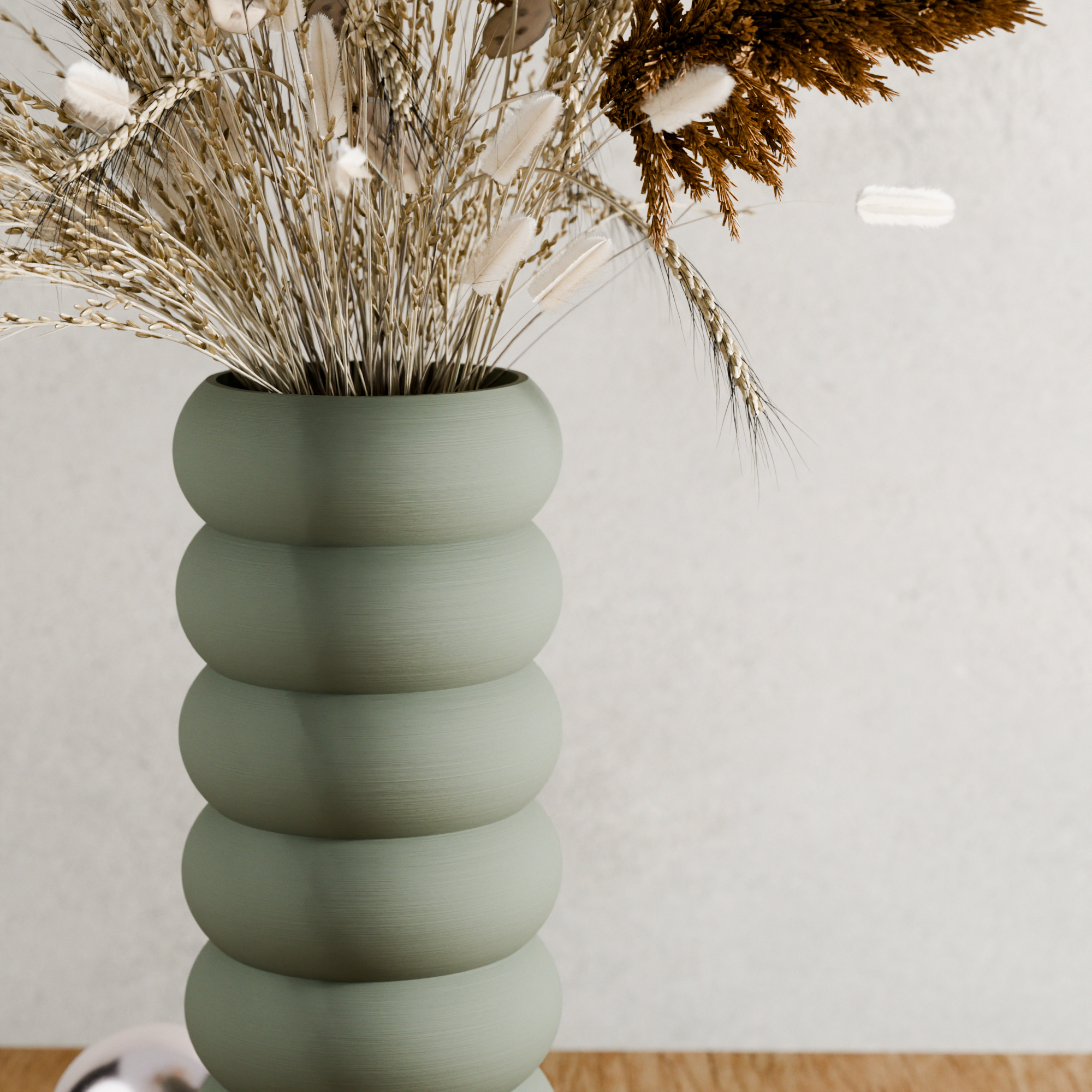 Green ribbed vase with dried plants on a light background