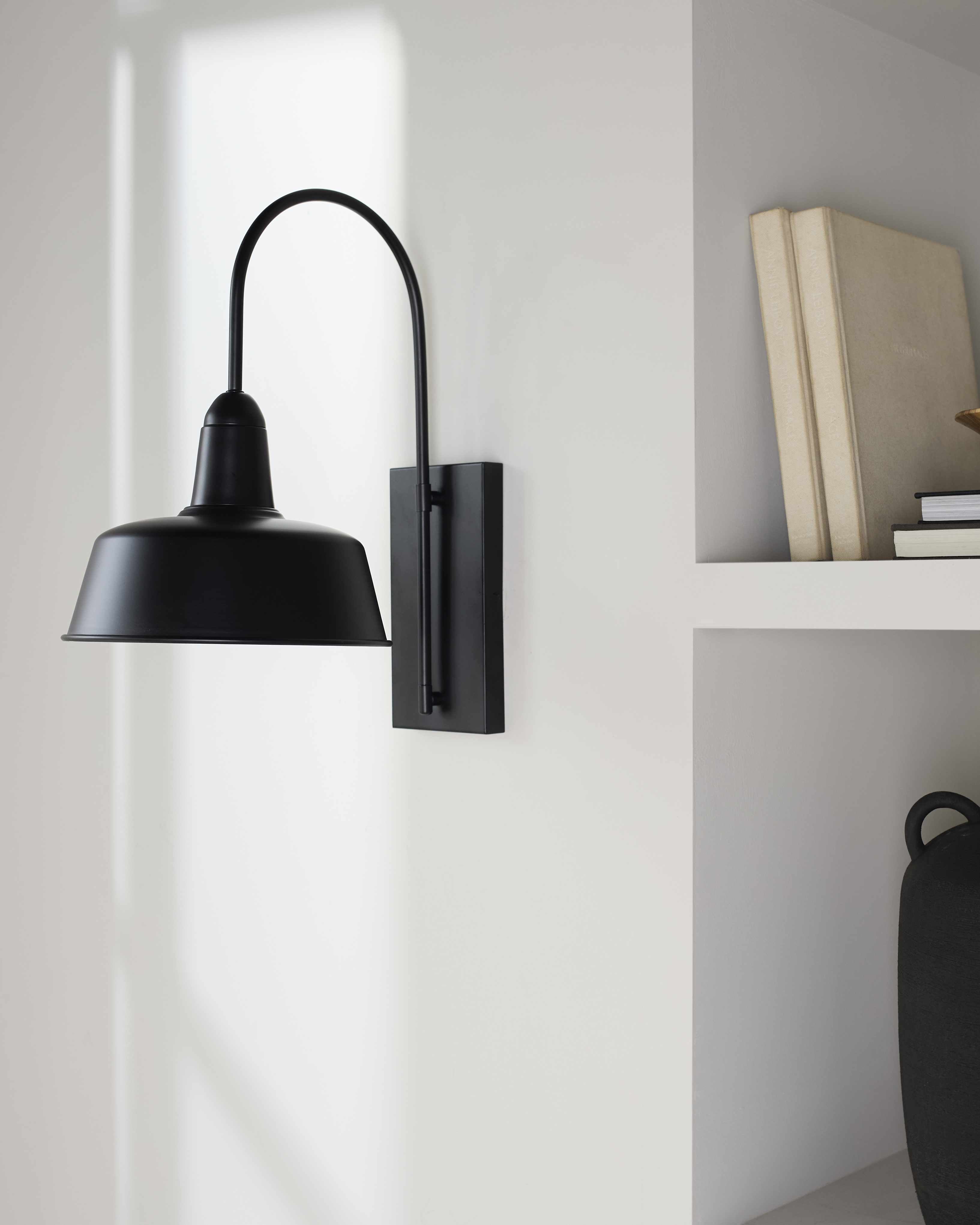 Black wall sconce on a white wall with books on a shelf in the background