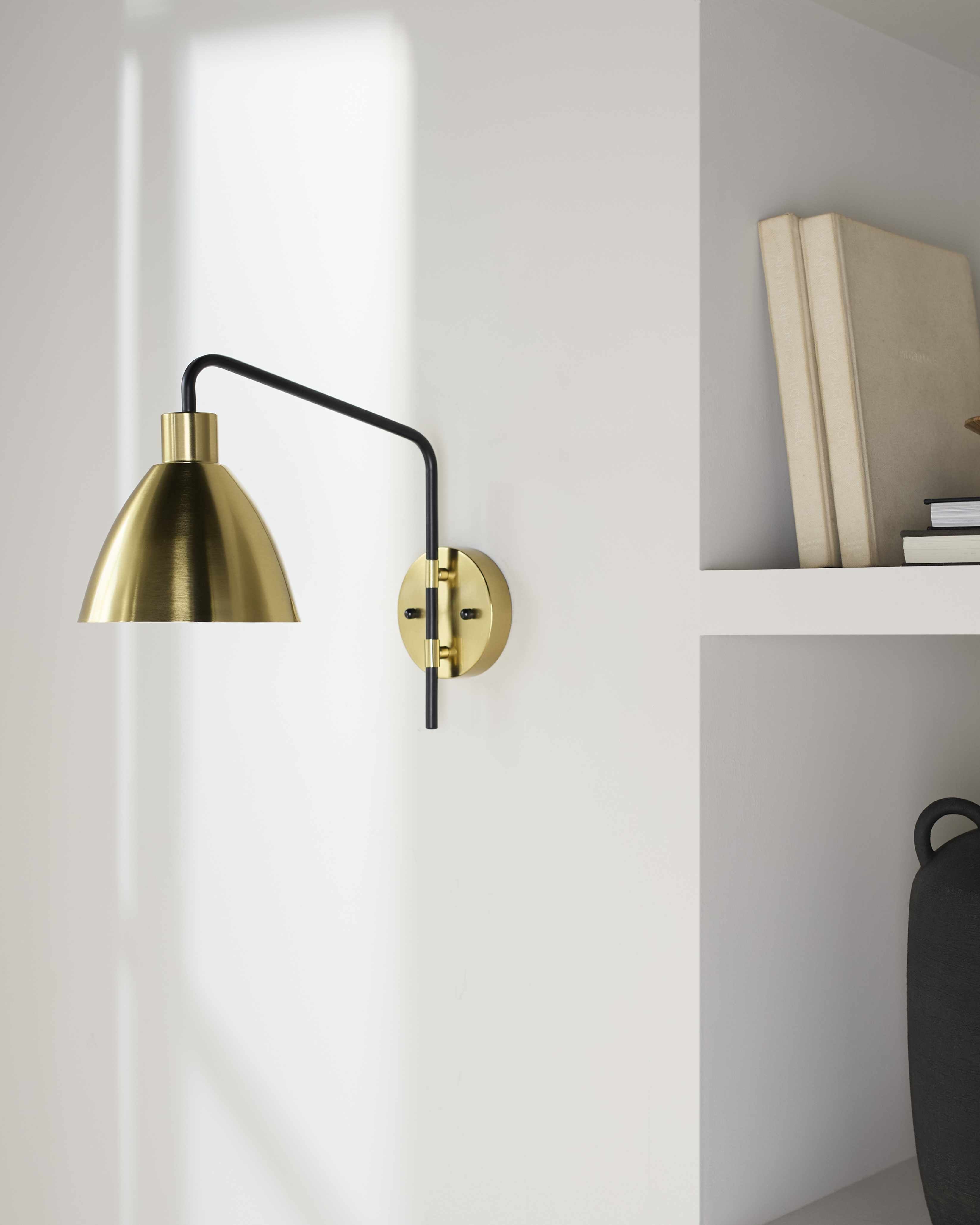 Gold wall lamp with black arm on a white wall
