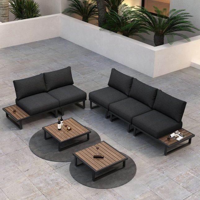 Outdoor patio furniture set with black cushions and wooden tables on a stone patio.