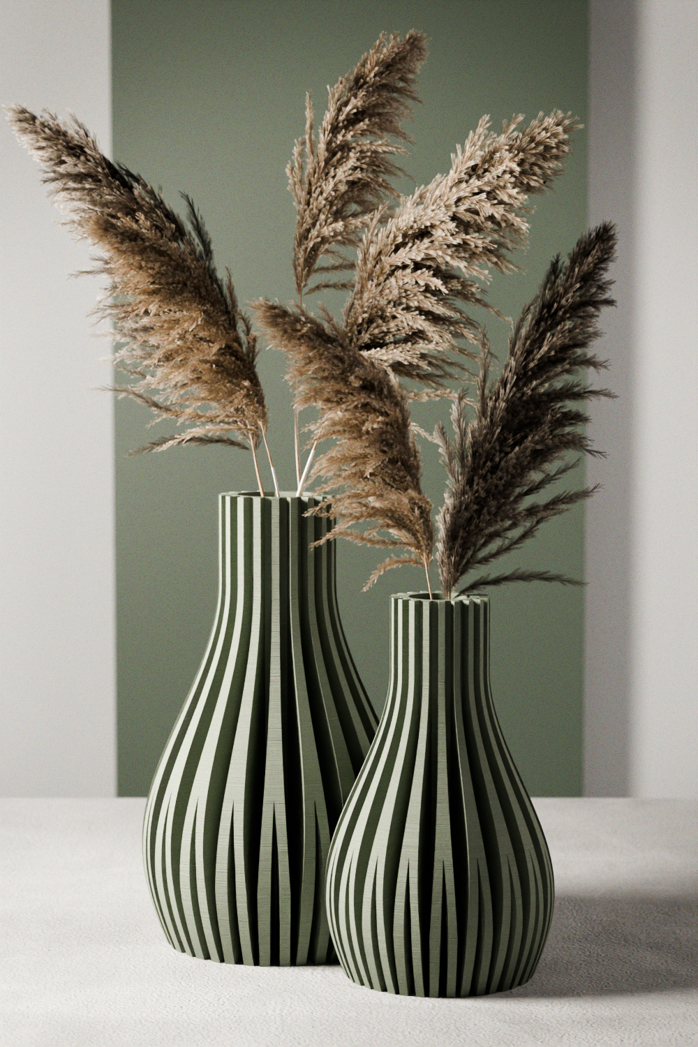 Two black and white striped vases with dried pampas grass against a green wall.