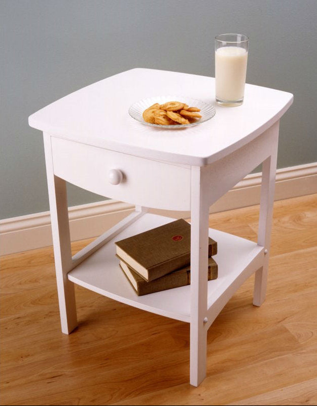 White side table with a glass of milk and cookies on a wooden floor.