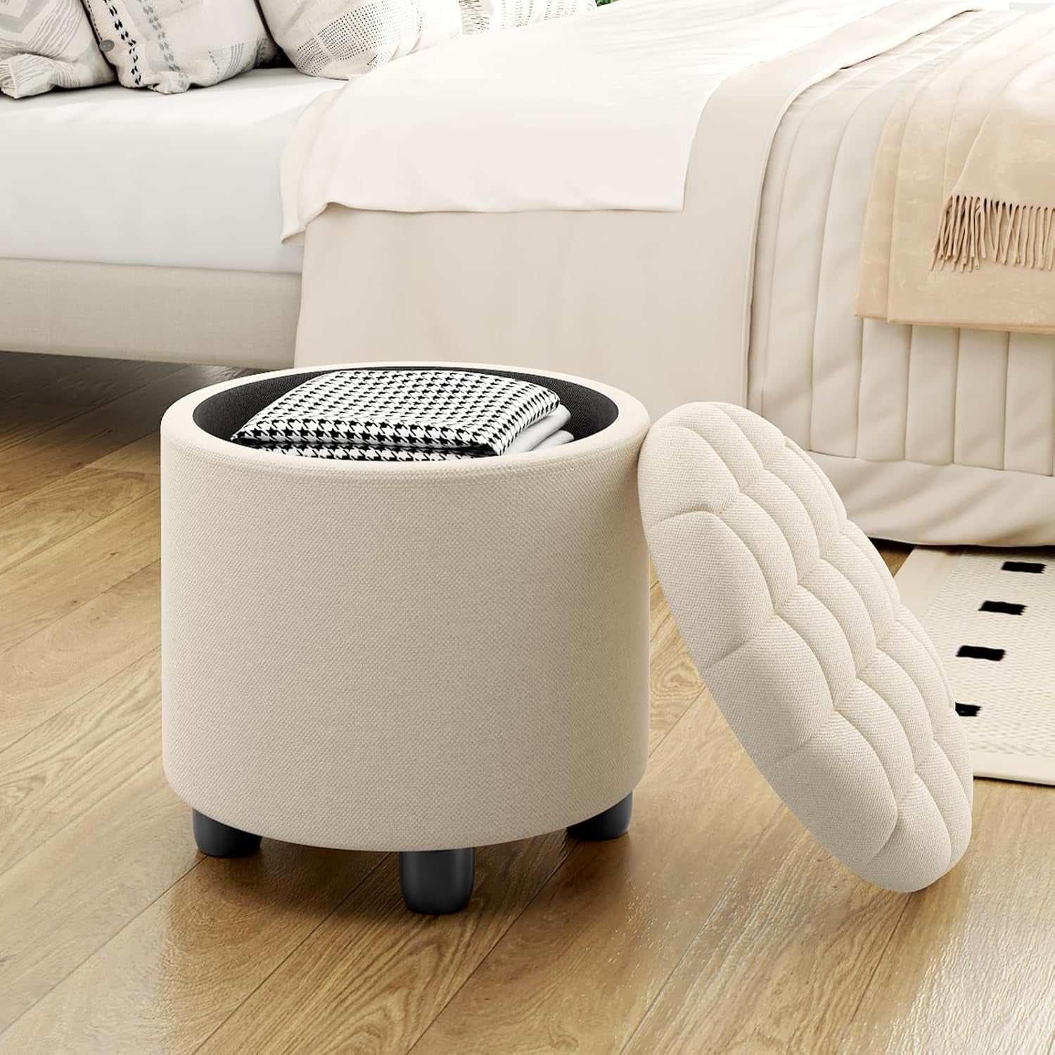 Round beige ottoman with a cushion on a wooden floor in a bedroom setting.