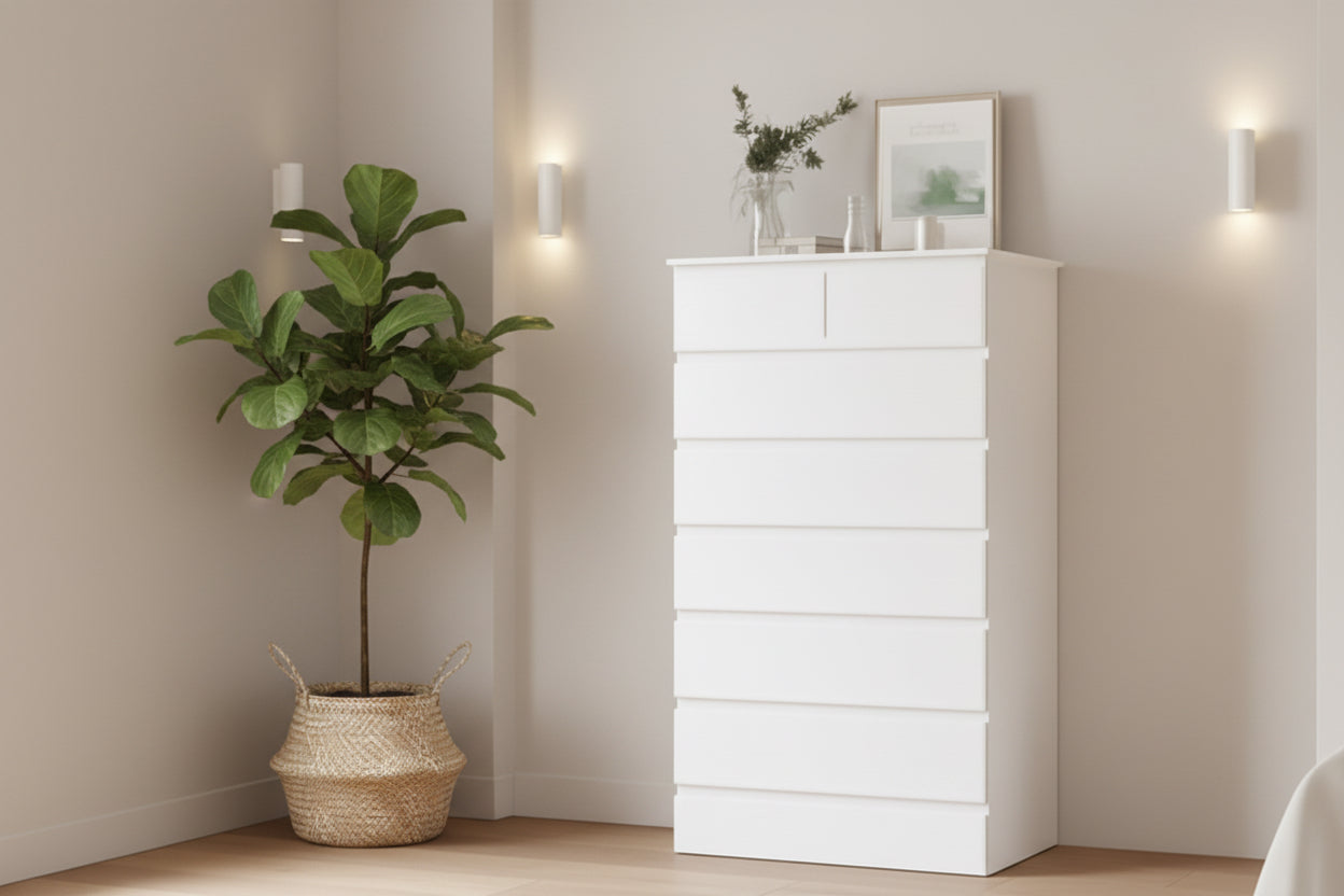 White dresser against a beige wall with a lamp and plant on a nightstand.