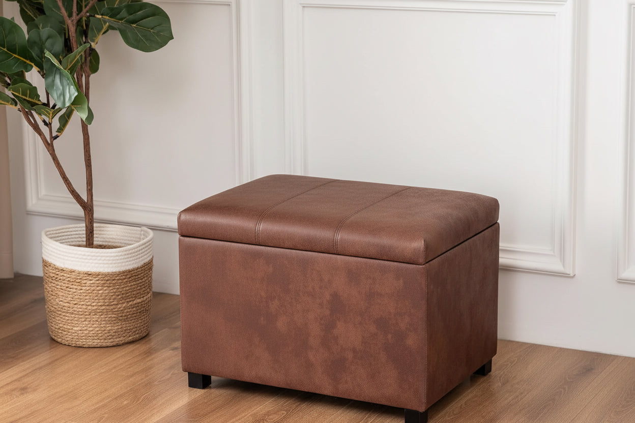 Person sitting on a brown storage ottoman in a room with a plant and white walls.