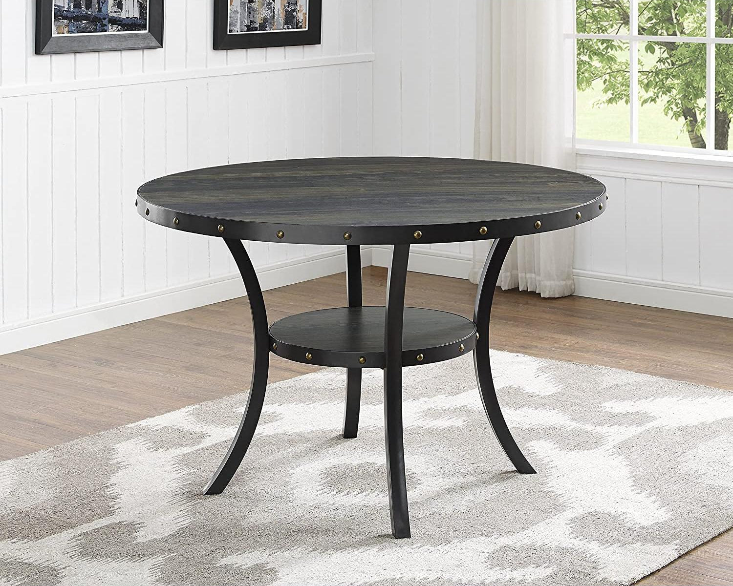 Round black dining table with metal accents in a room with a window and framed pictures on the wall.