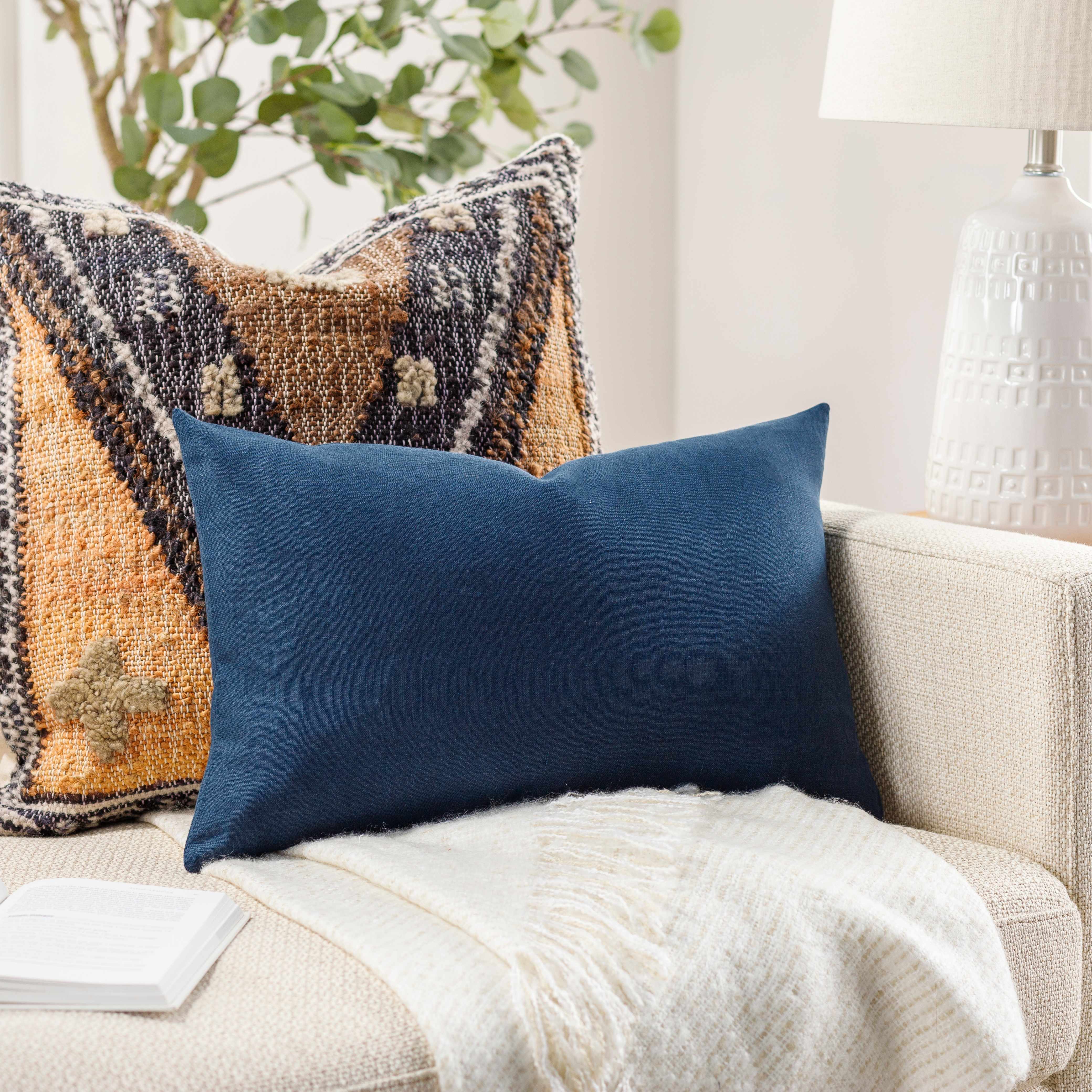 Navy blue pillow on a beige sofa with a textured orange pillow and white lamp in the background.