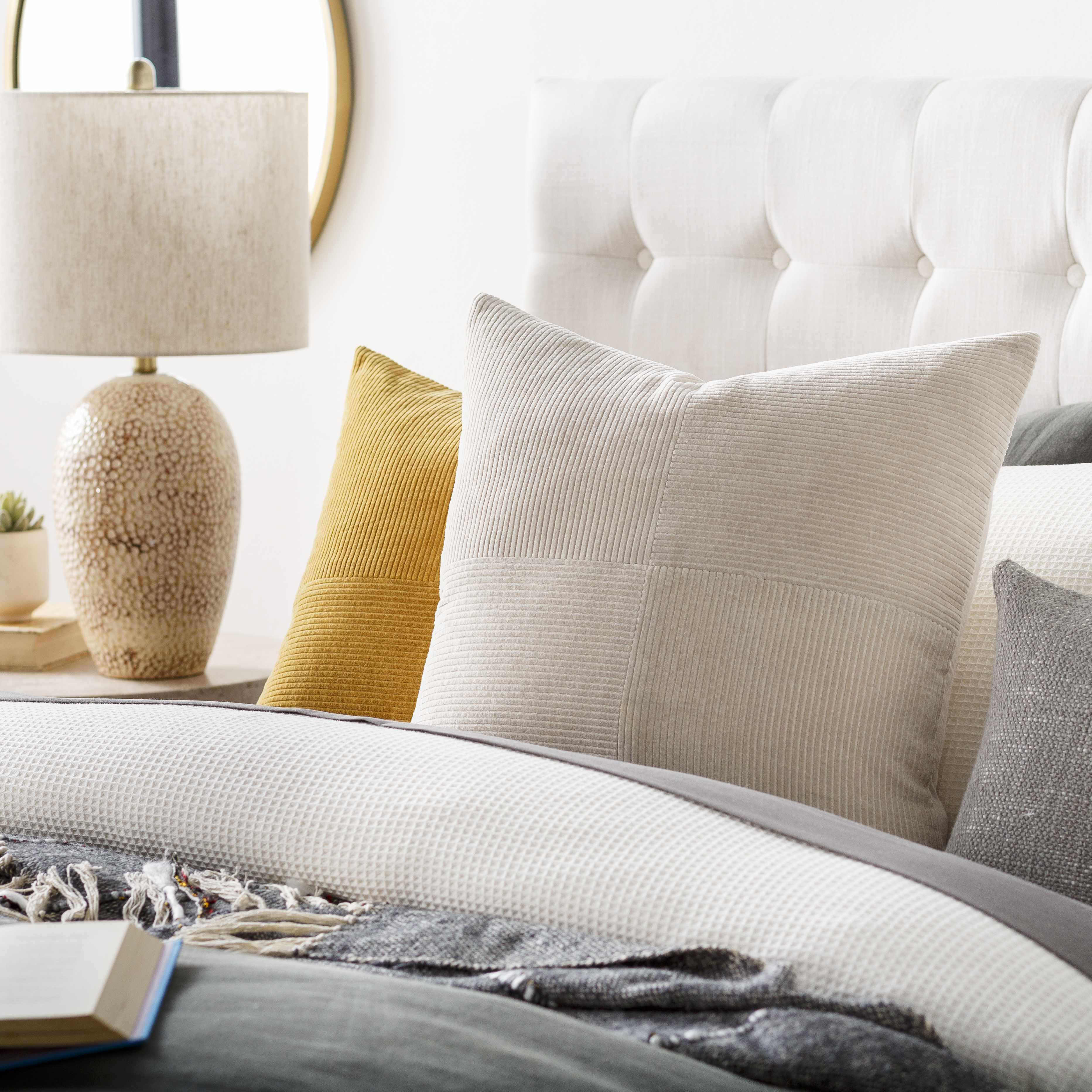 Neatly arranged pillows on a bed with a lamp and decor items in the background.