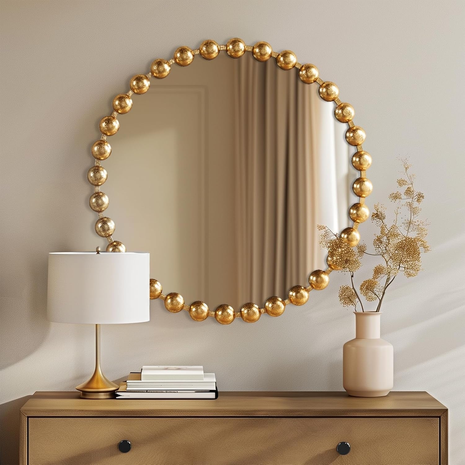 Round mirror with gold spherical frame on a wall above a wooden console table with decor items.
