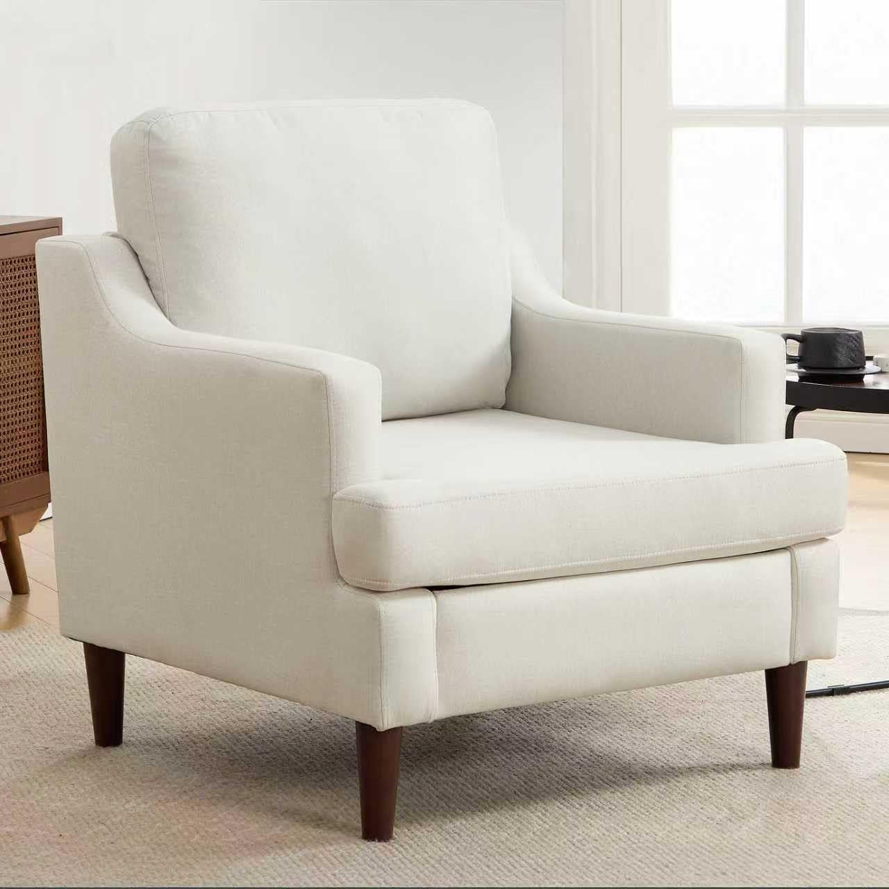 White armchair with wooden legs in a room with large windows.