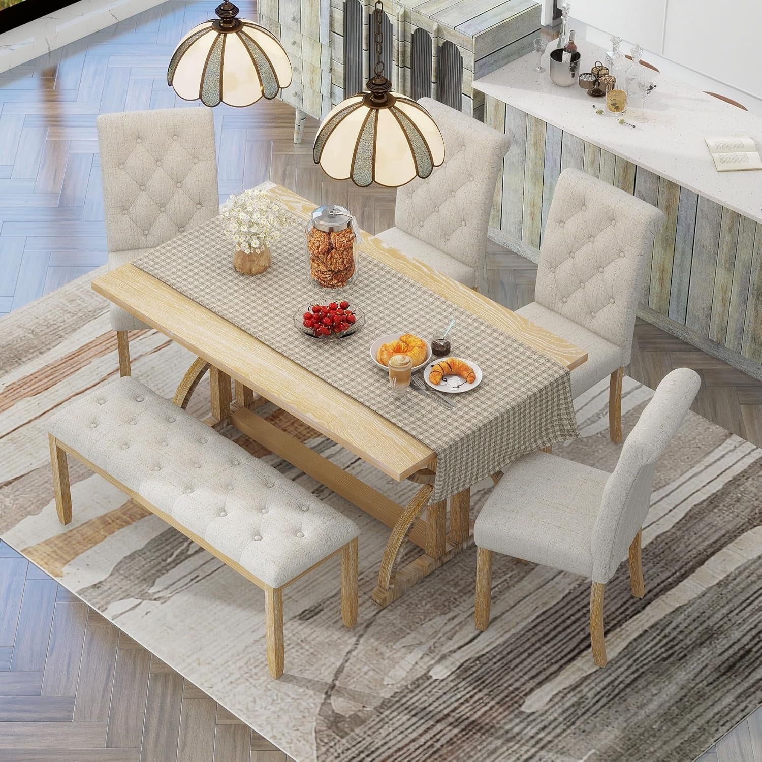 Dining table set with chairs and a bench on a checkered tablecloth, with a kitchen in the background.