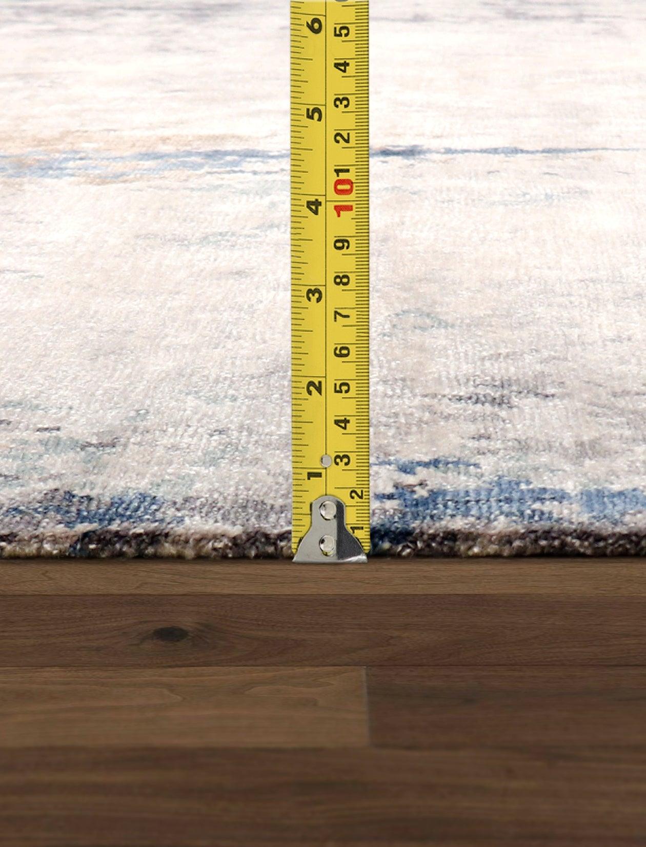 Rug on a wooden floor with a measuring tape indicating its size.