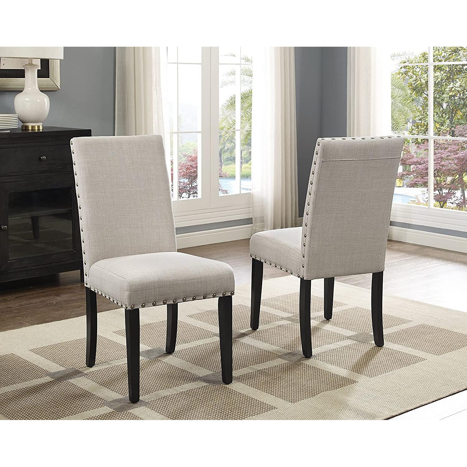 Two beige upholstered chairs with black legs in a room with large windows.