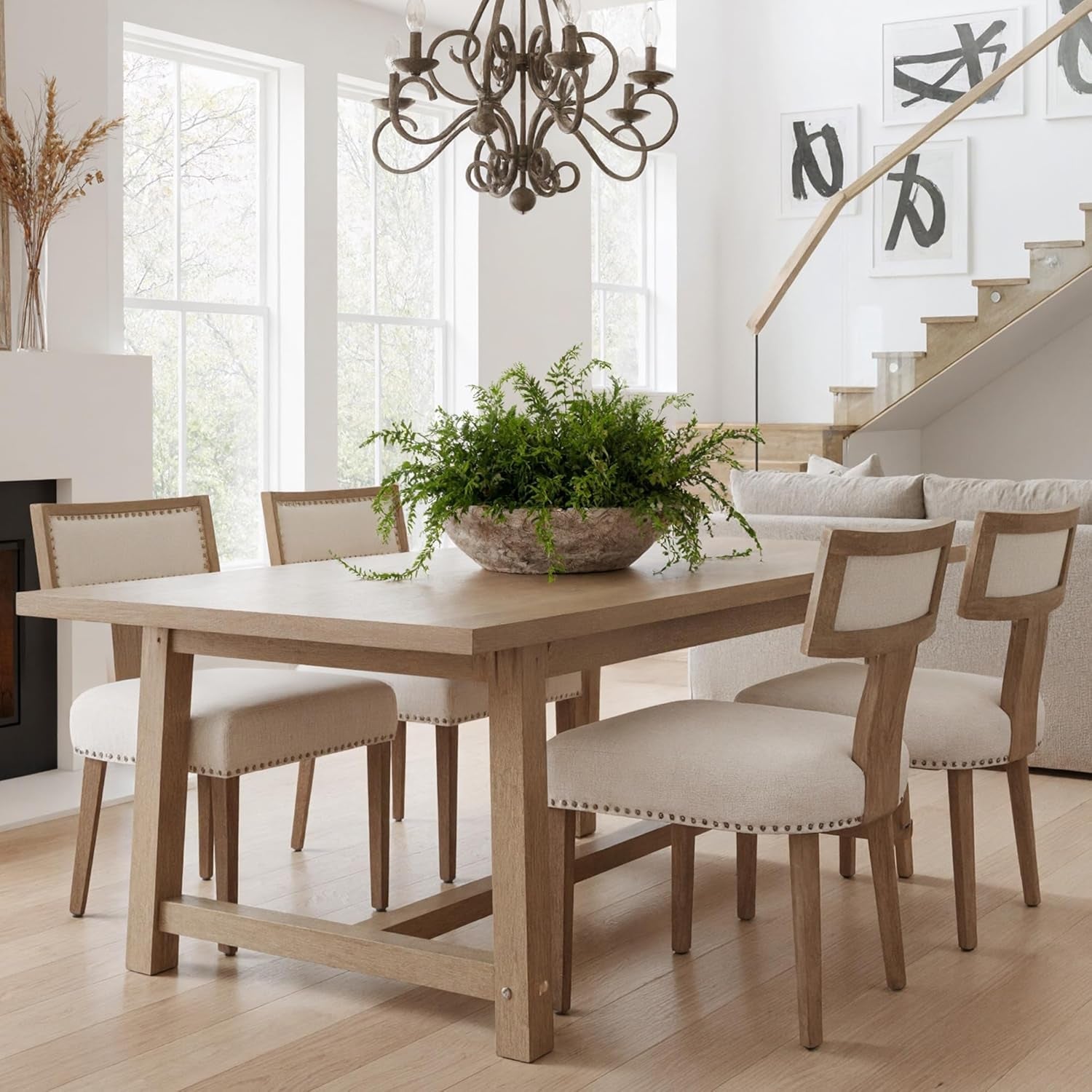 Dining room with wooden table and chairs, potted plant, and staircase in the background.