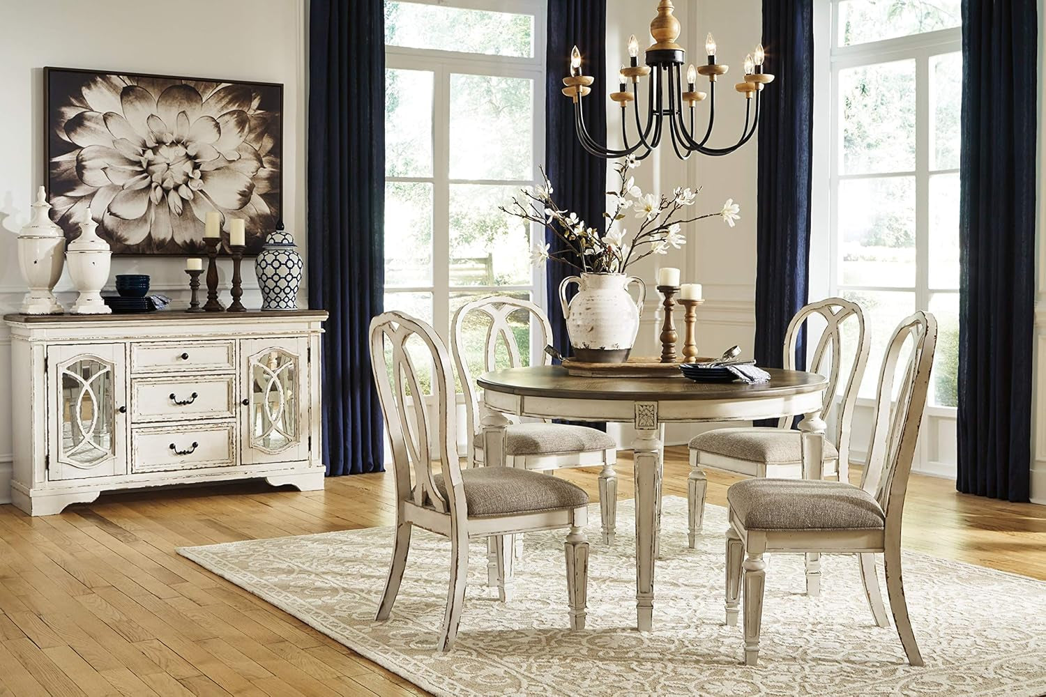 Dining room with round table and chairs, sideboard, and large windows.