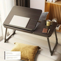 Foldable laptop desk on a sofa with a cup, notebook, and pen.