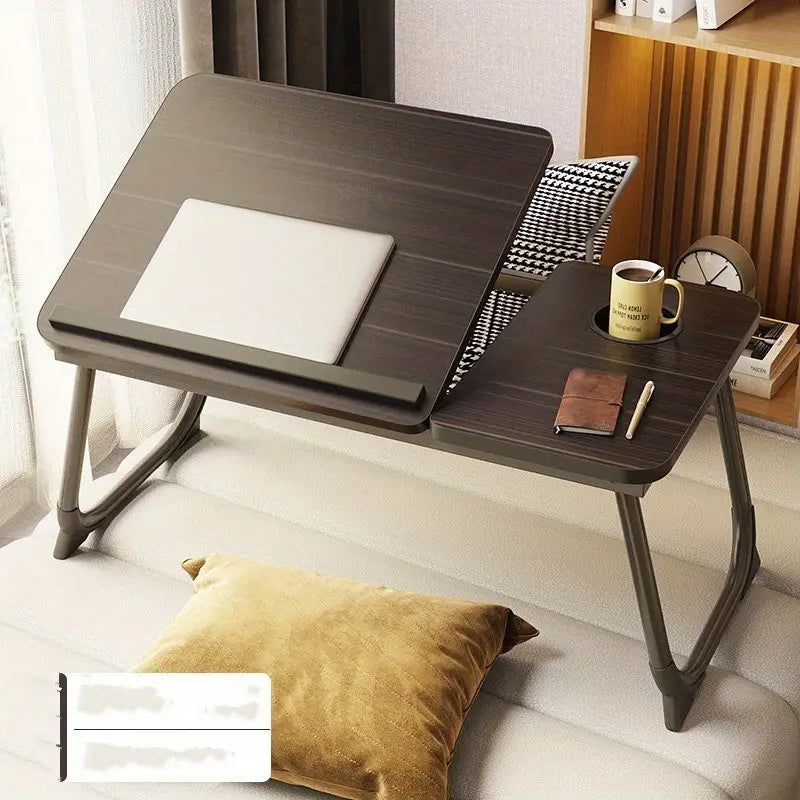 Foldable laptop desk on a sofa with a cup, notebook, and pen.