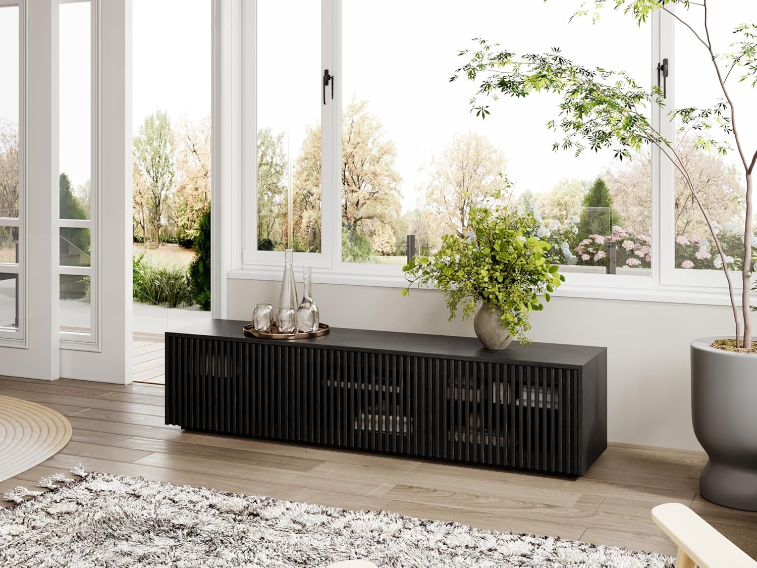Modern black entertainment console against a wall with large windows and decorative plants.