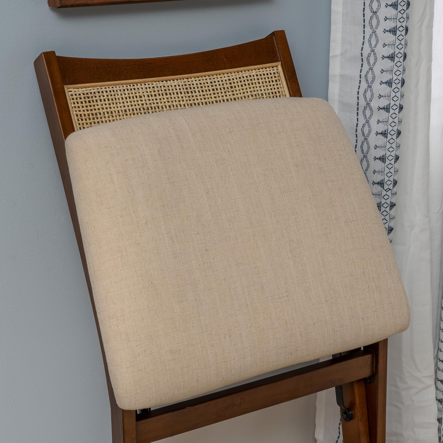 Chair with beige cushion and wooden frame against a light blue wall.