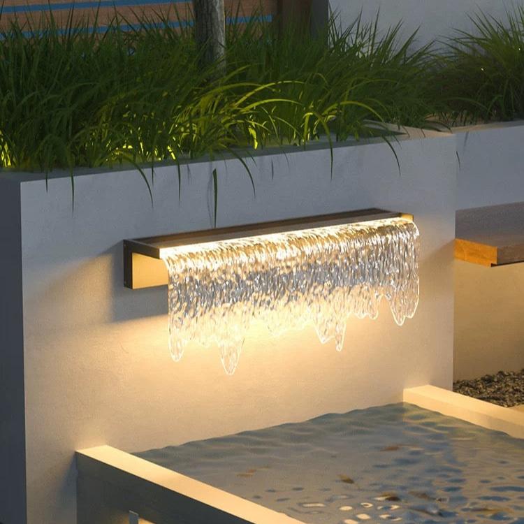 Modern outdoor wall light fixture with water feature effect on a white wall.