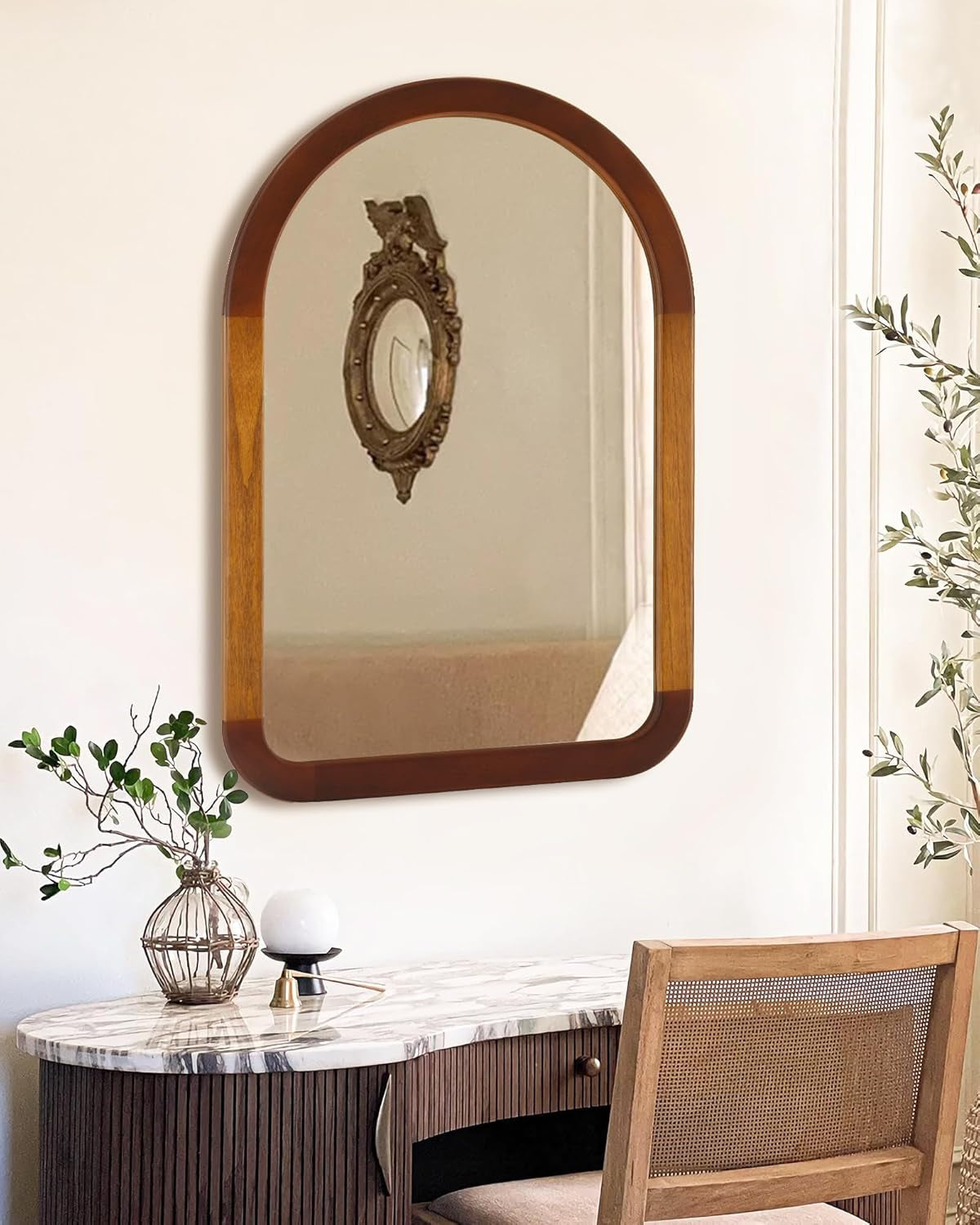Wooden mirror with decorative frame on a wall above a marble table with a chair.