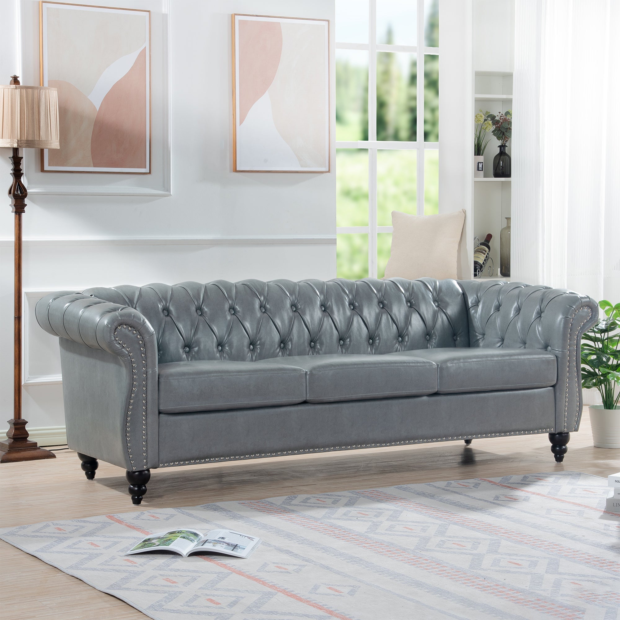 Gray tufted sofa in a living room setting with a lamp, rug, and window in the background.