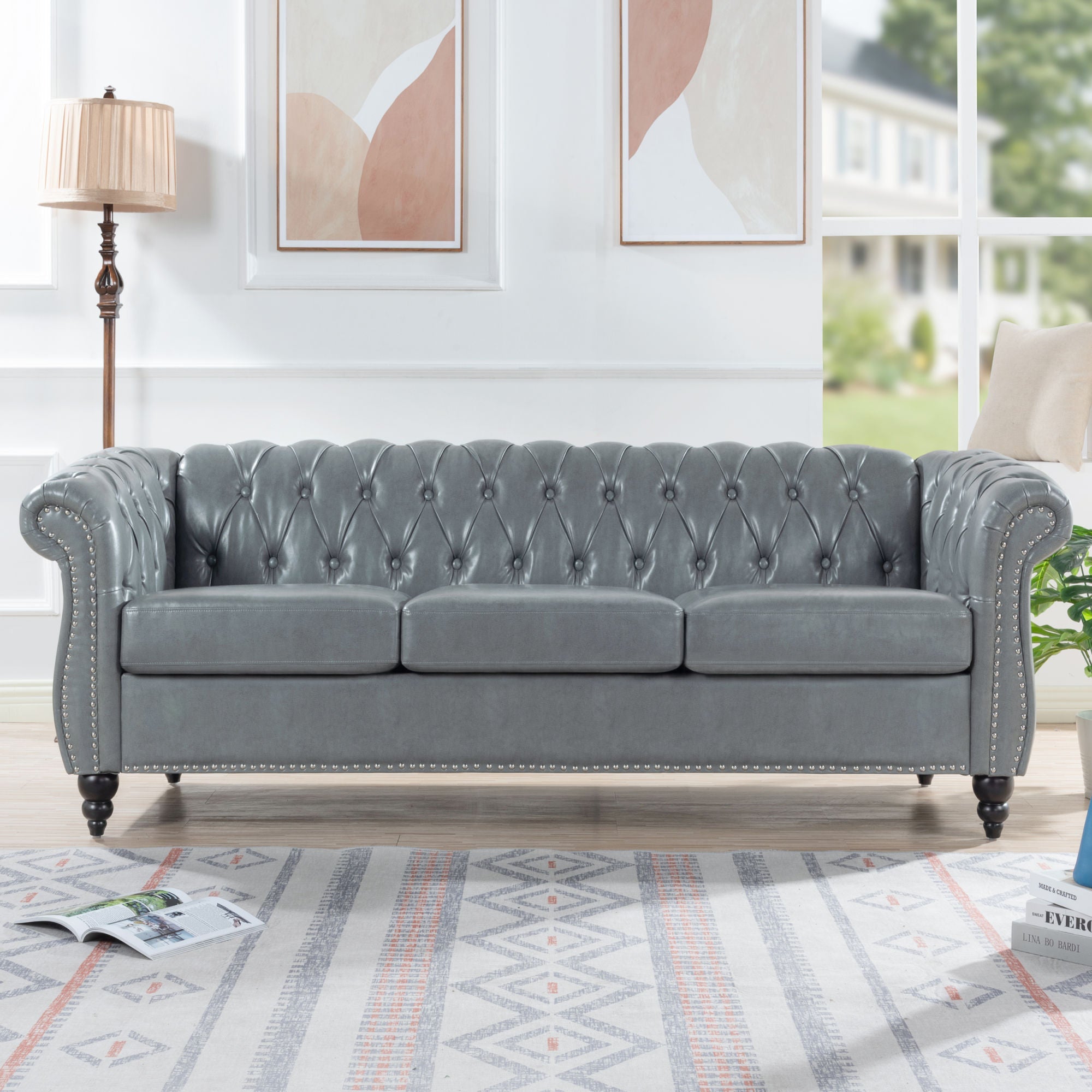 Gray tufted sofa in a living room setting with abstract art and a lamp.