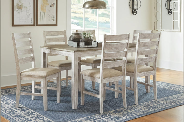 Dining room table set with chairs on a blue patterned rug, coastal or modern farmhouse theme.