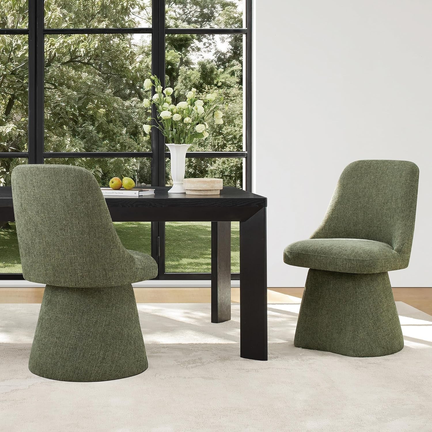 Two green chairs around a black dining table with a vase of flowers in a room with large windows.
