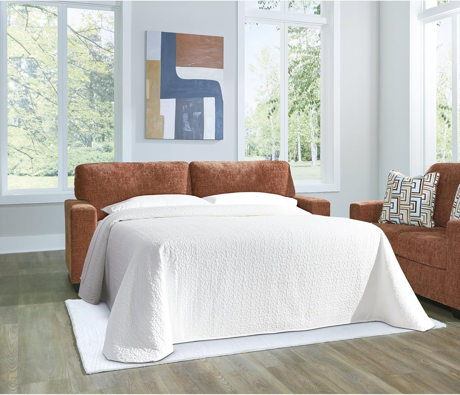 Brown sectional sofa with a white blanket in a room with large windows.