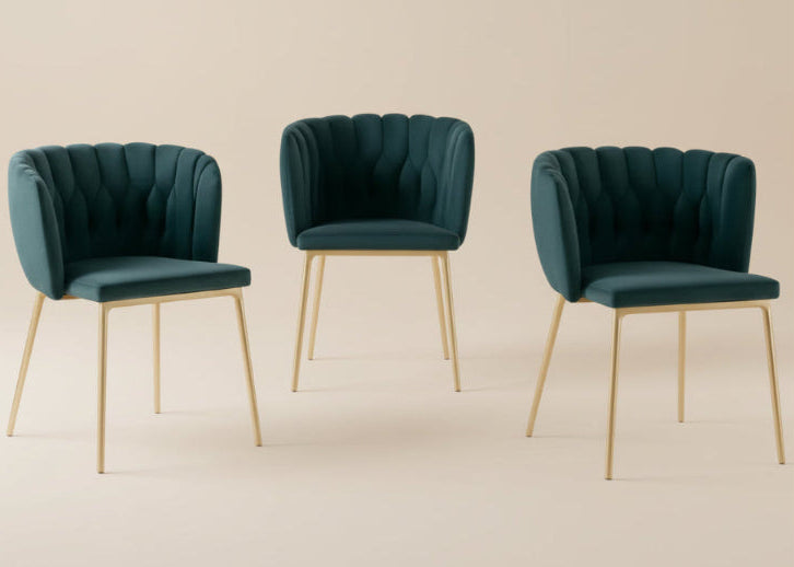 Three teal chairs with gold legs in a room with a beige wall and lamp.