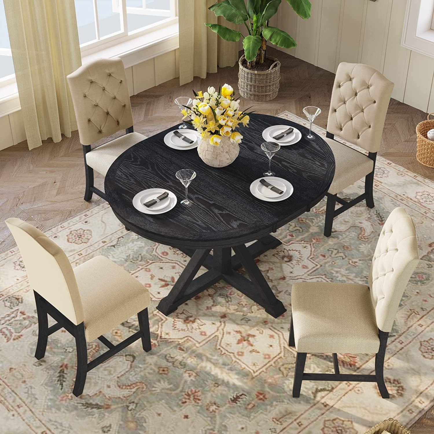 Round black dining table with four beige chairs in a room with large windows and a plant.