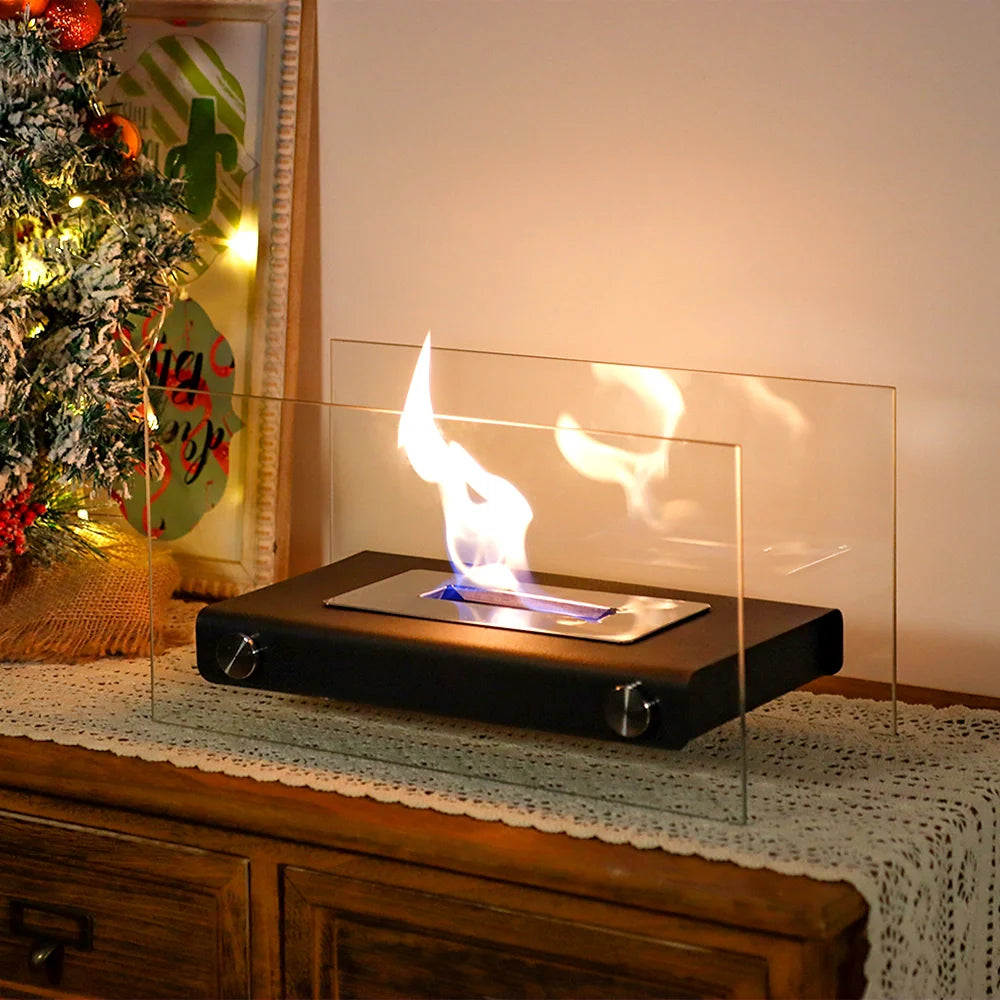 Tabletop fireplace with flames on a wooden surface next to a decorated Christmas tree.