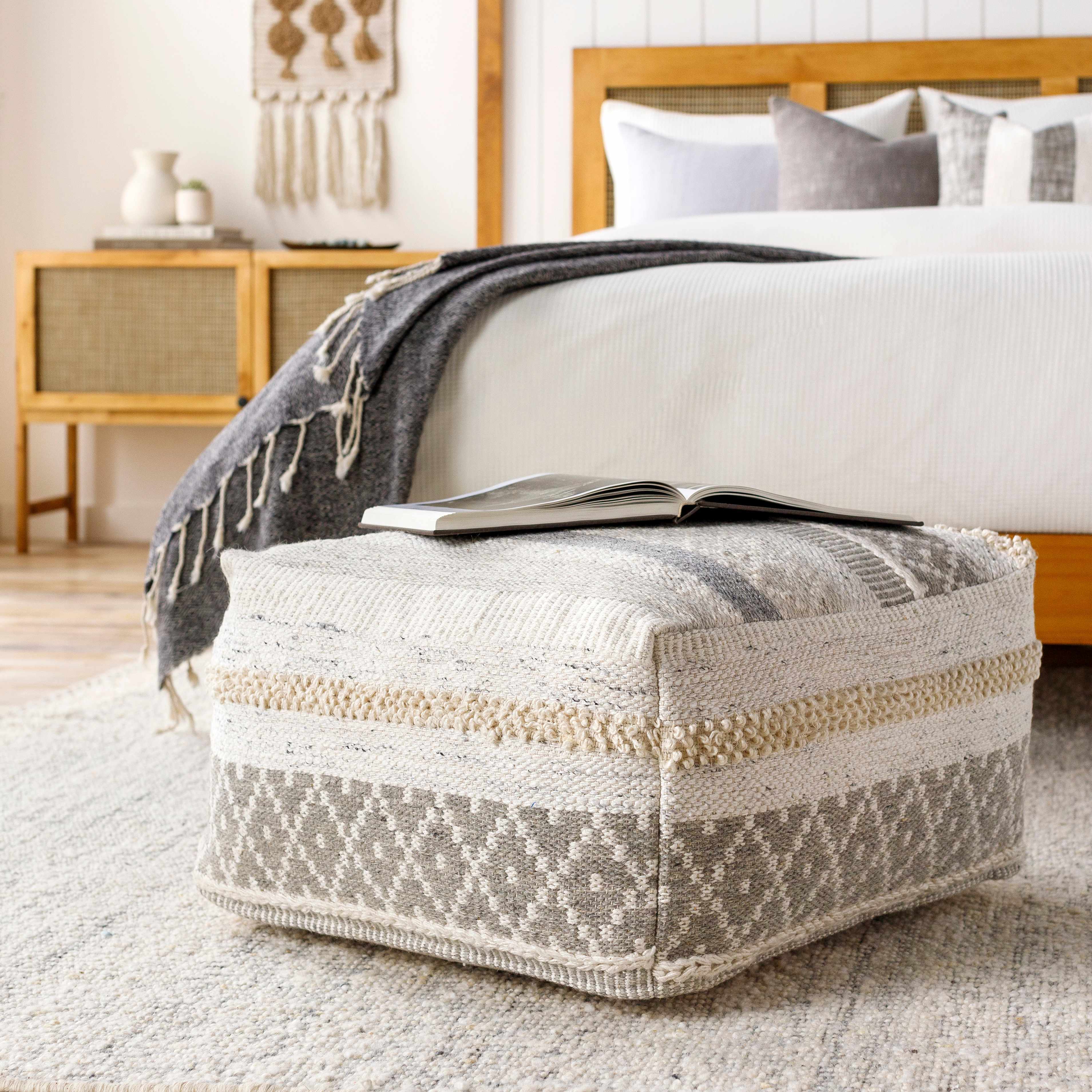 Patterned ottoman in a bedroom with a bed and nightstand in the background