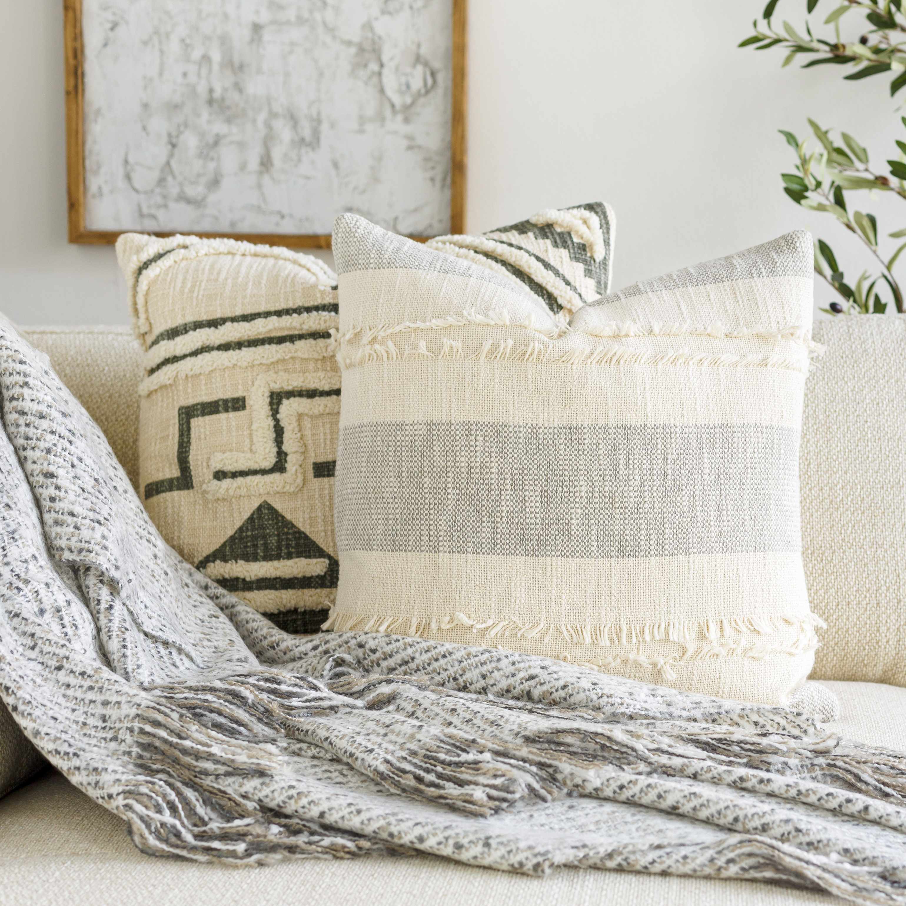 Decorative pillows on a sofa with a textured blanket and framed artwork in the background.