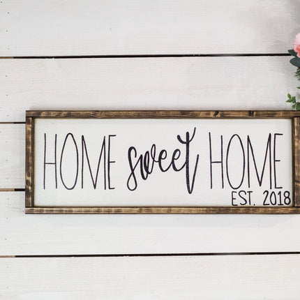 Decorative sign with 'Home sweet home est. 2018' on a white wooden background with flowers.