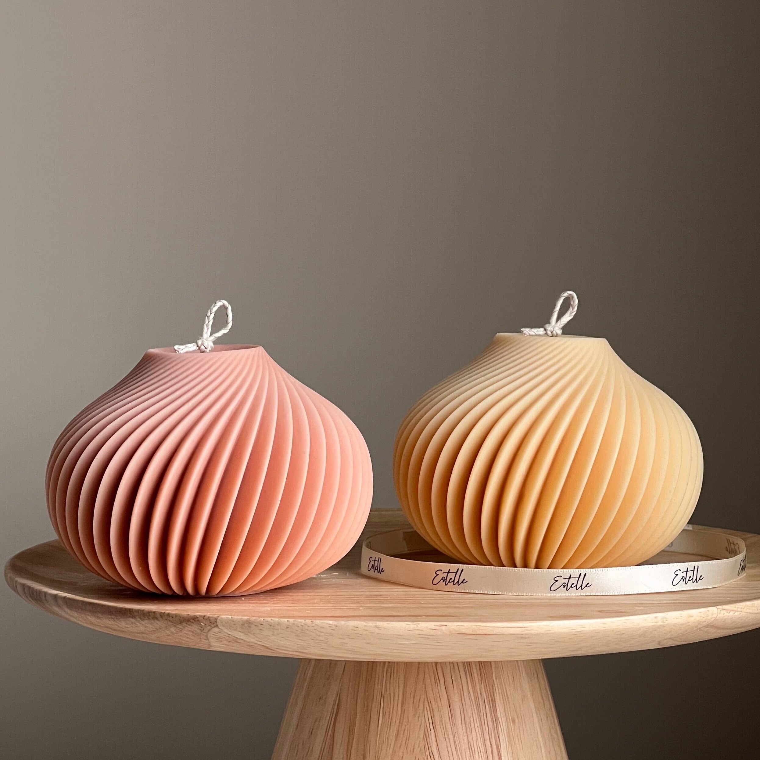 Two ribbed ceramic vases, one pink and one beige, on a wooden stand with a neutral background.