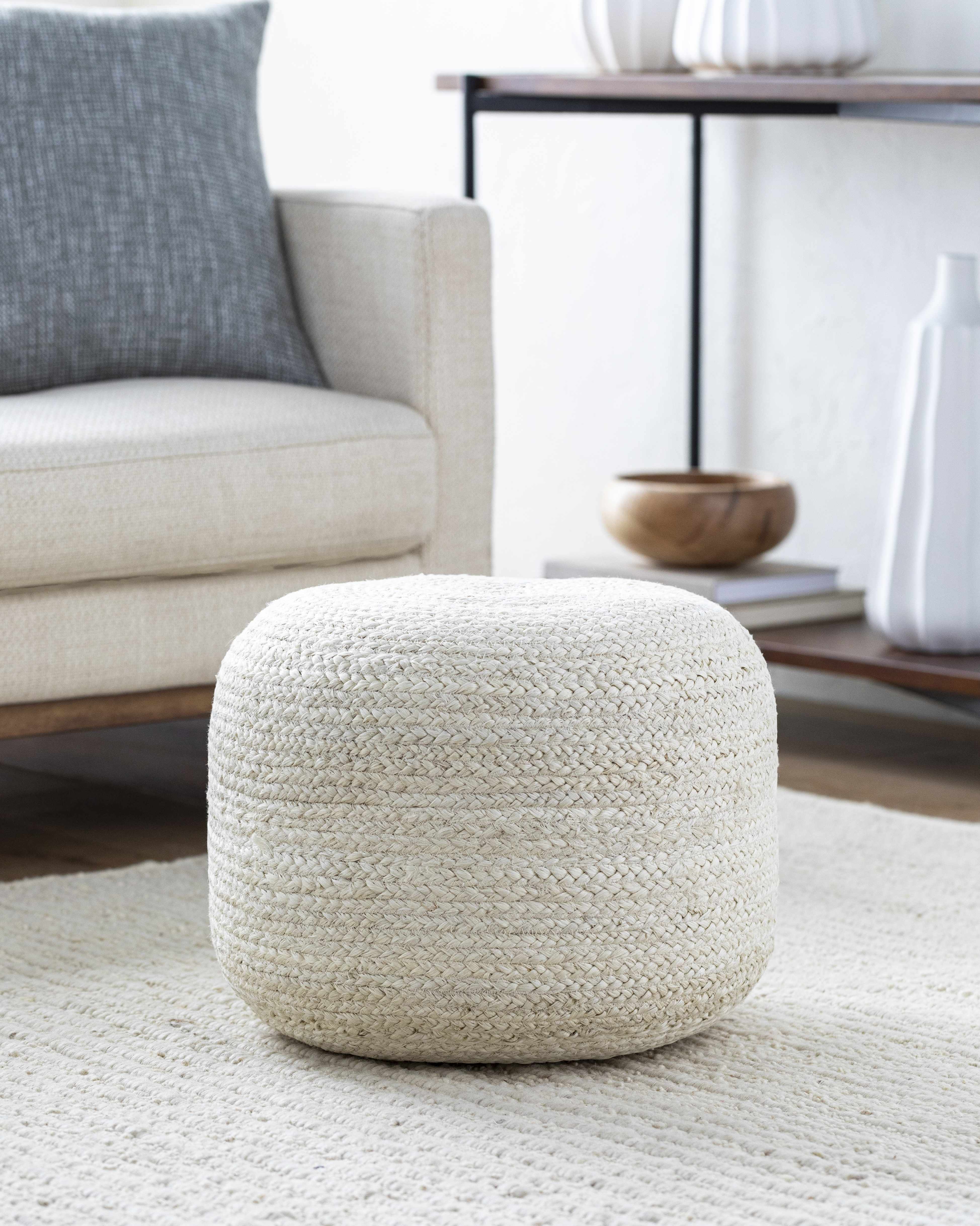 White woven ottoman in a living room setting with a couch and coffee table.