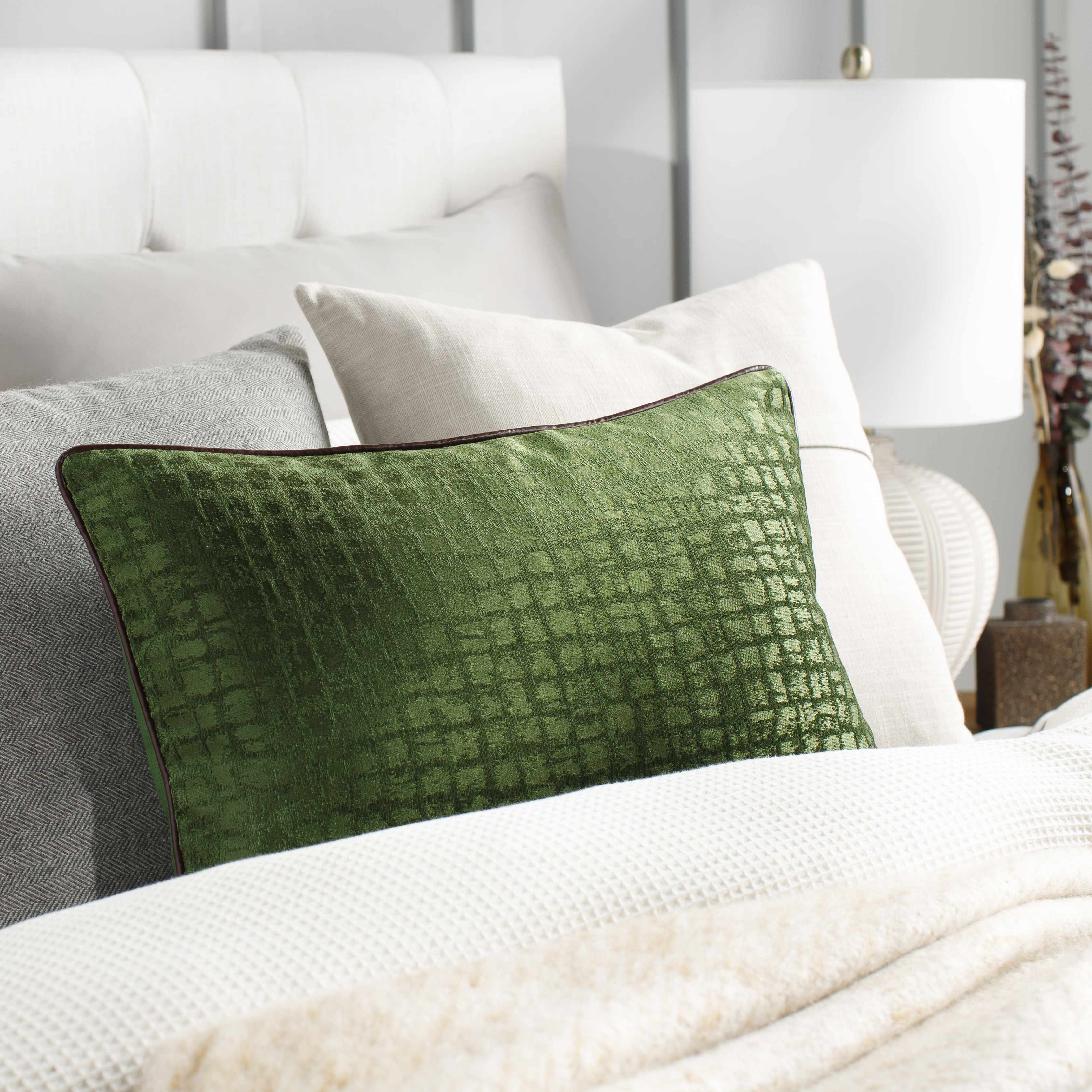 Green textured pillow on a bed with neutral bedding and lamp in the background